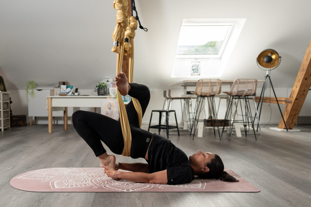 Femme pratique le yin yoga aérien avec un tissu accroché au plafond.